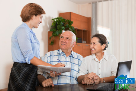 Mature couple answer questions of outreach worker with notebook in office