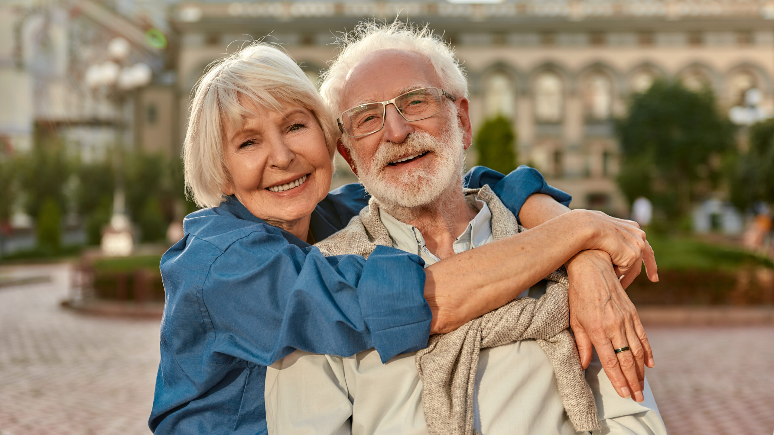 I love my husband. Portrait of cheerful senior couple in casual clothing embracing each other and looking at camera with smile while standing together outdoors